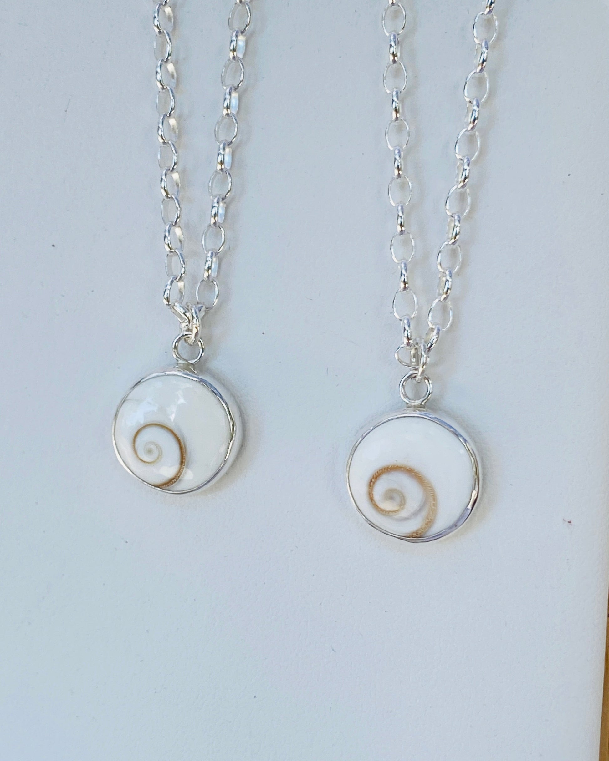 Two silver necklaces with circular pendants featuring round Shiva Eye spiral stones 