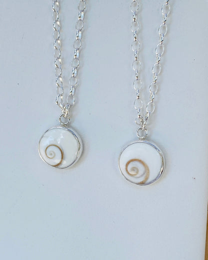 Two silver necklaces with circular pendants featuring round Shiva Eye spiral stones 